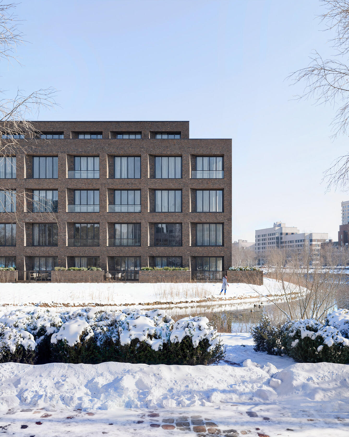 Rendering of a modern brick residential building in a snowy landscape with a person walking by a frozen pond