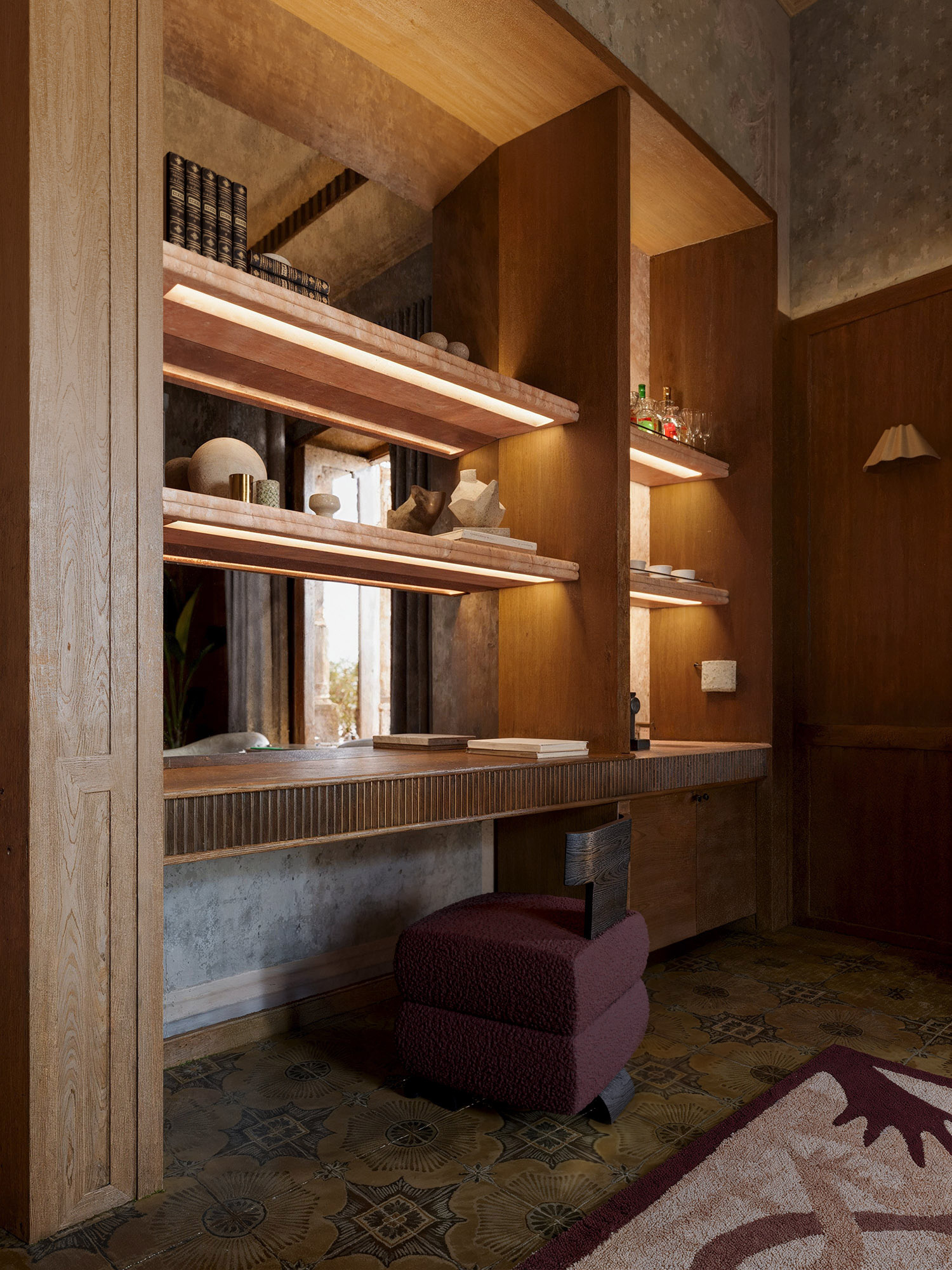Interior Design Rendering of a Built-in wooden vanity with illuminated marble shelves, sculptural decor, and a textured burgundy stool on vintage-patterned tile flooring—blending classic charm with modern elegance.