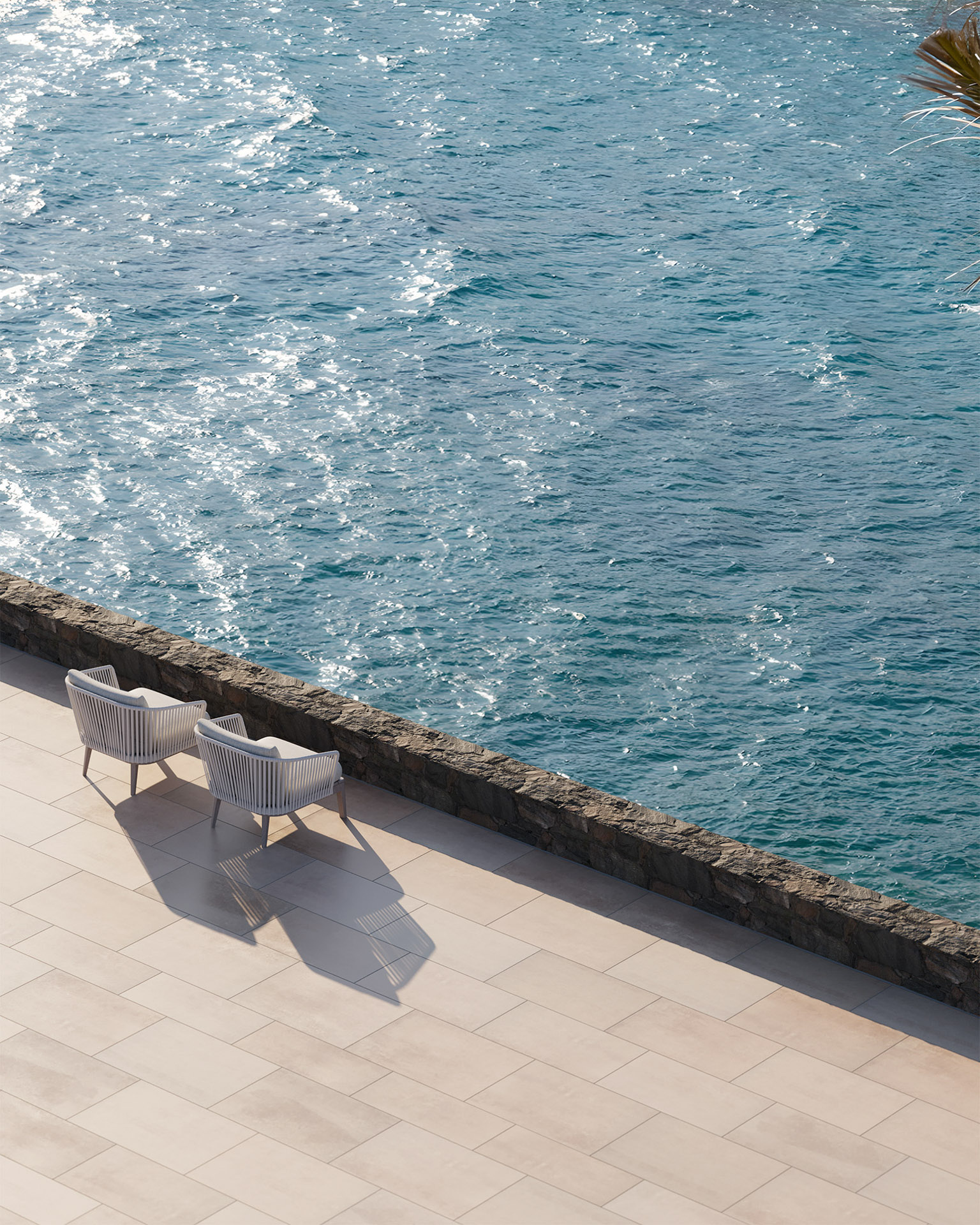Photoreal Rendering of two lounge chairs on a tiled terrace overlooking sparkling blue sea, bordered by a stone wall.