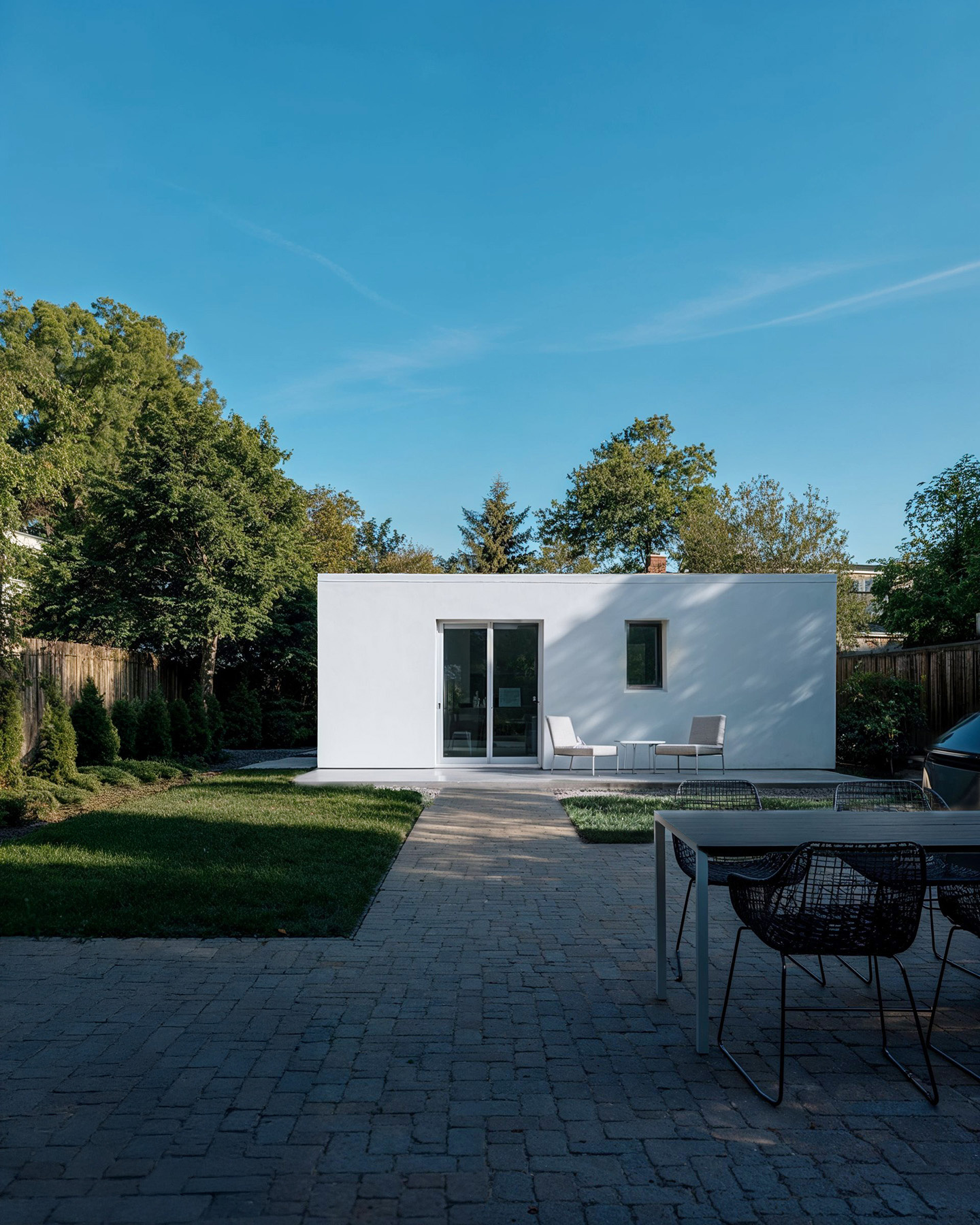 A rendering of a manufactured home in a suburban backyard with pacing and a lawn and a dog walking. There are trees, a blue sky, and a backyard BBQ area.