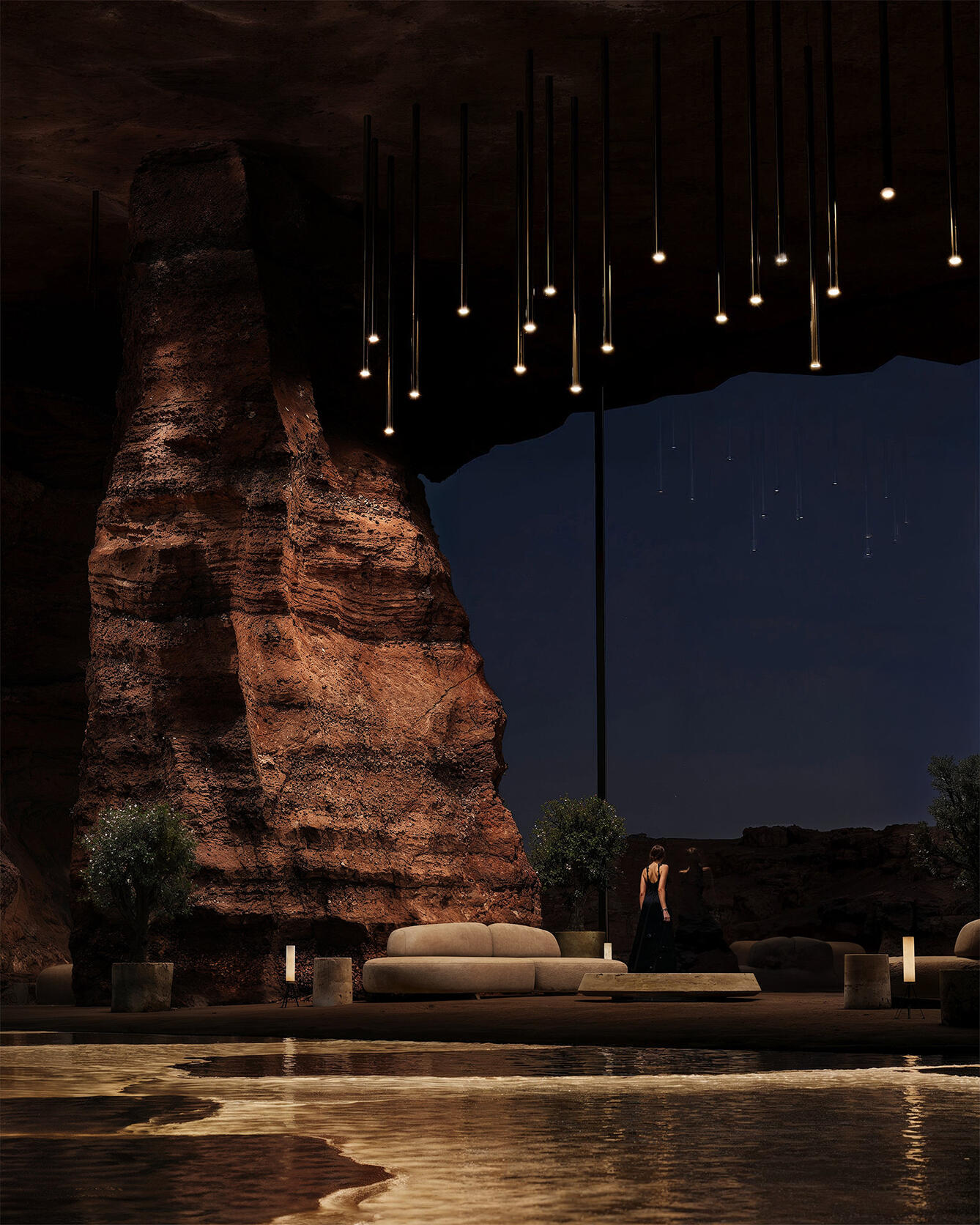 A dramatic lounge space set within a cavernous rock formation, featuring suspended pendant lights, sculptural furniture, and a reflective pool that glows softly under ambient lighting.