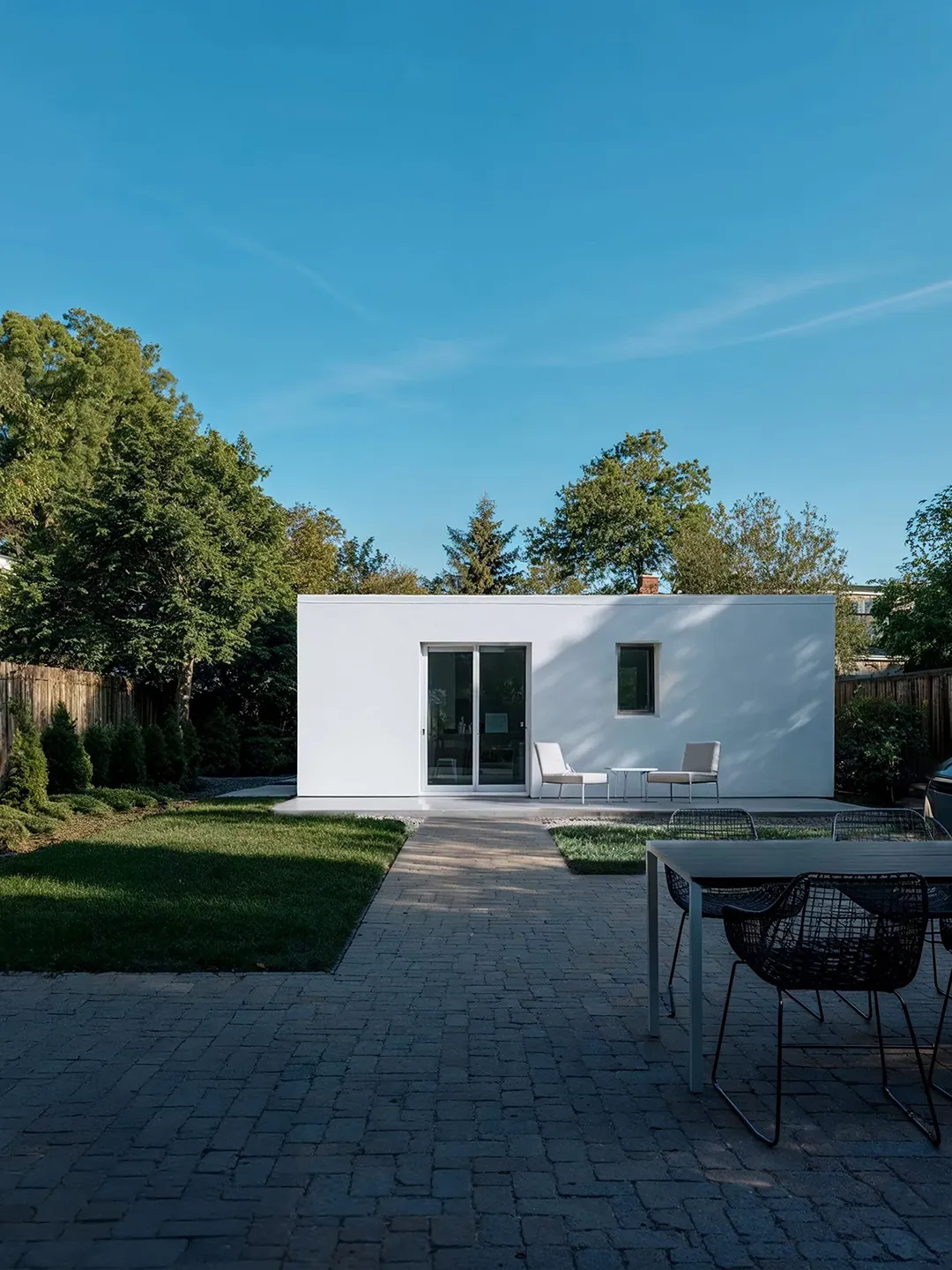 Garden Studio — Minimalist Residential Exterior Rendering White flat-roof garden studio with sliding glass doors in tree-lined suburban backyard — residential architecture rendering