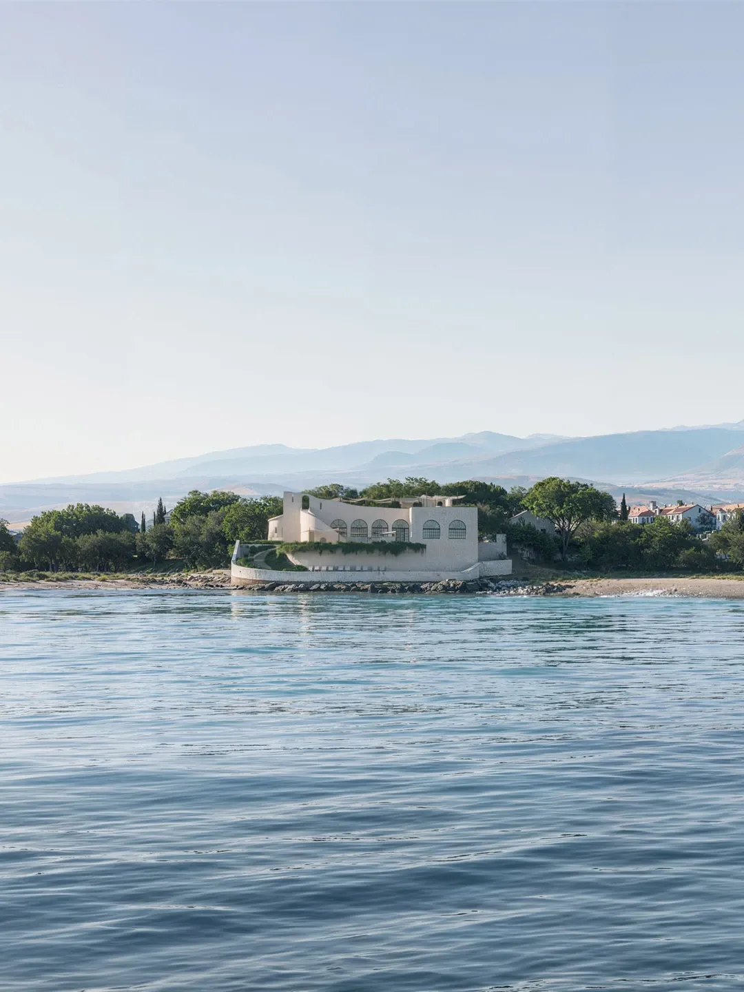Cream Mediterranean villa with arched arcade facade and rooftop planting on rocky coastal promontory — architectural exterior rendering